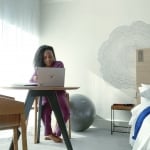 Woman sitting at a table look at laptop next to a window in hotel room