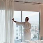 woman stares out of window in white bathrobe